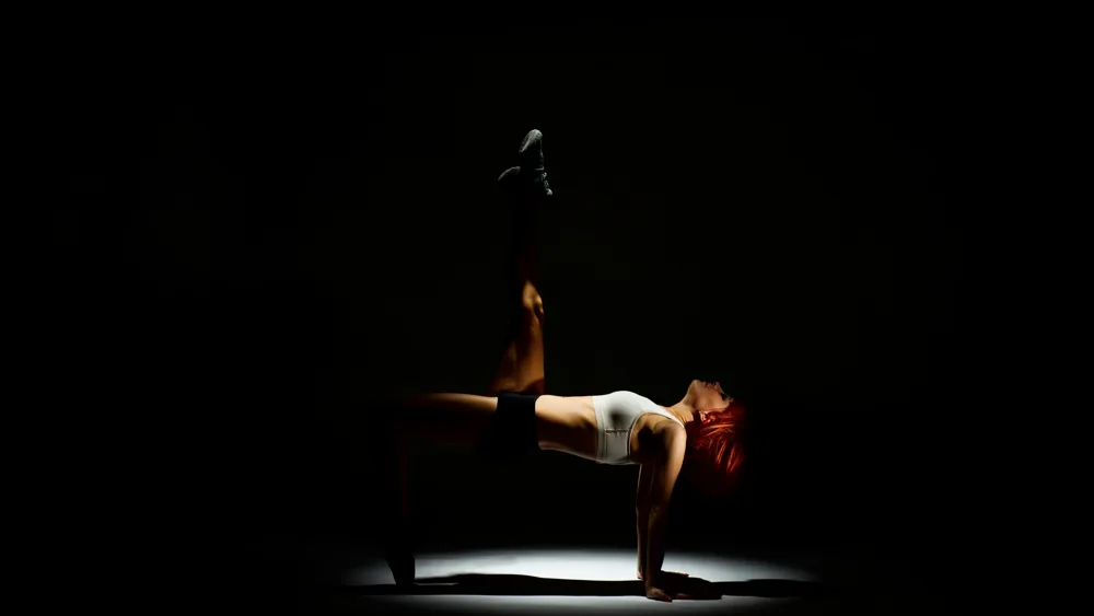 A floor-based strength pose in a dark, focused training setting